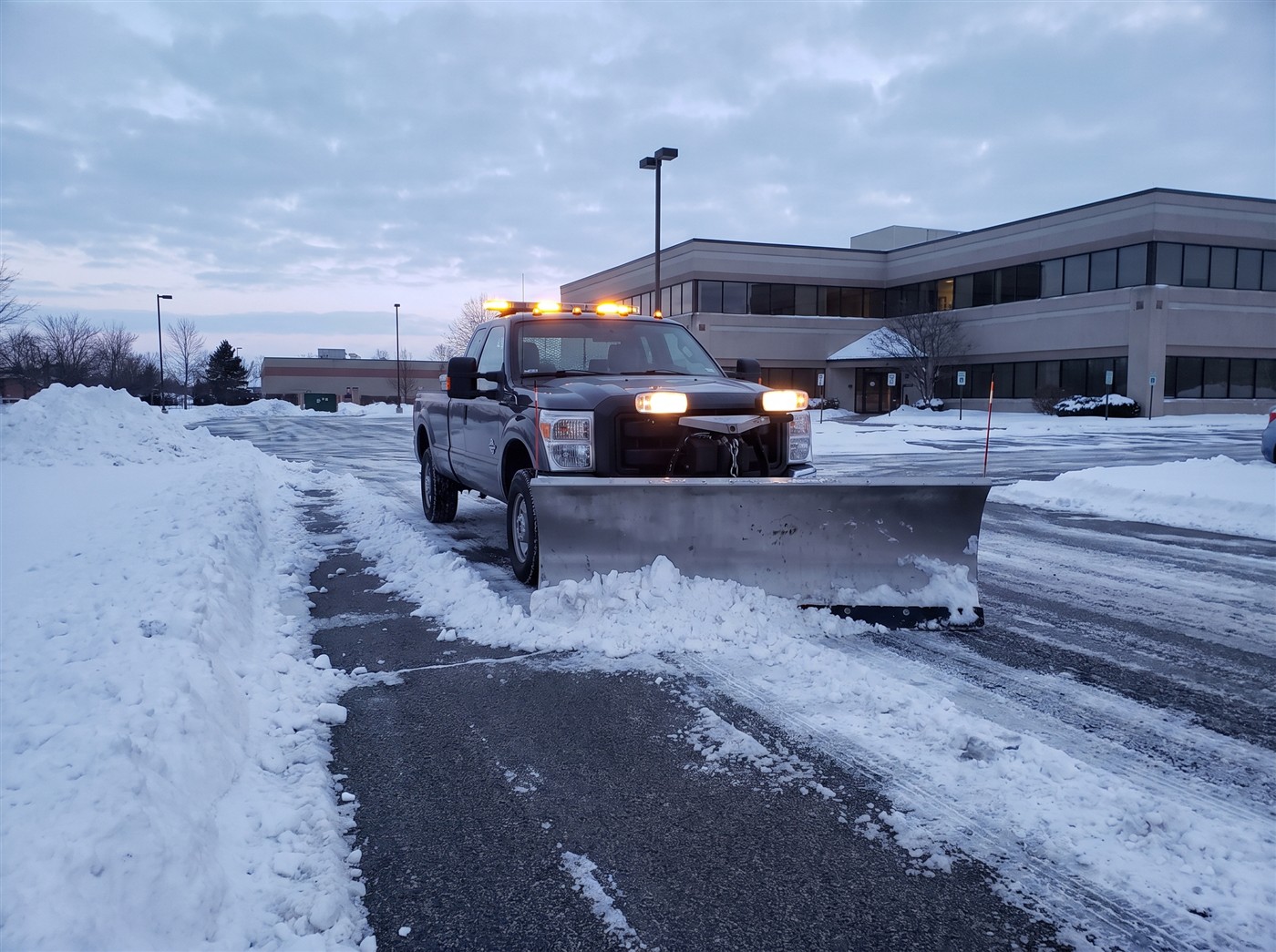 A plow truck clearing a commercial parking lot at dawn